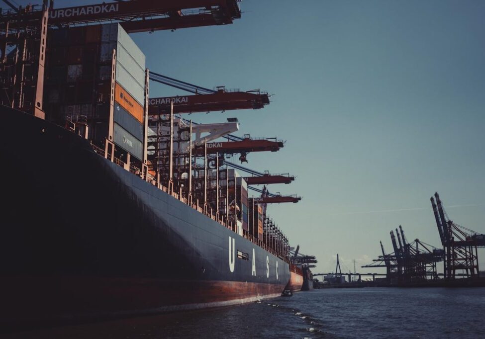 A large cargo ship docked at Hamburg Harbor, cranes loading containers under a clear sky.