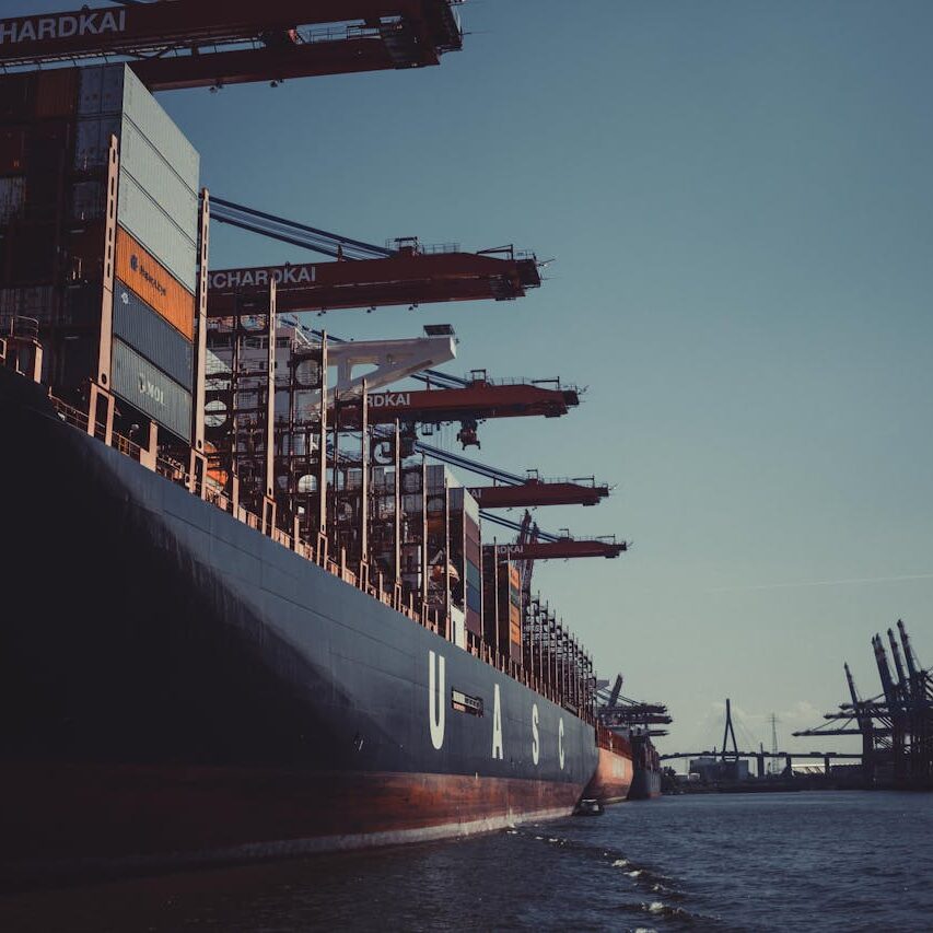A large cargo ship docked at Hamburg Harbor, cranes loading containers under a clear sky.